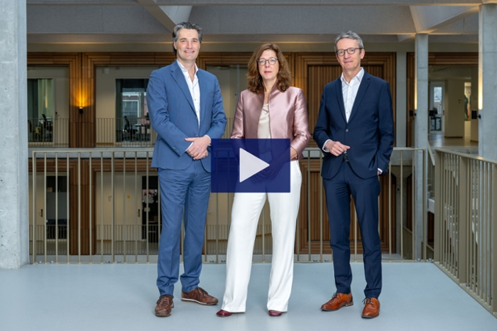 Three board members, a woman flanked by two men, pose in a modern office environment.